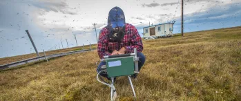 a man squatting in a field programming measuring equipment